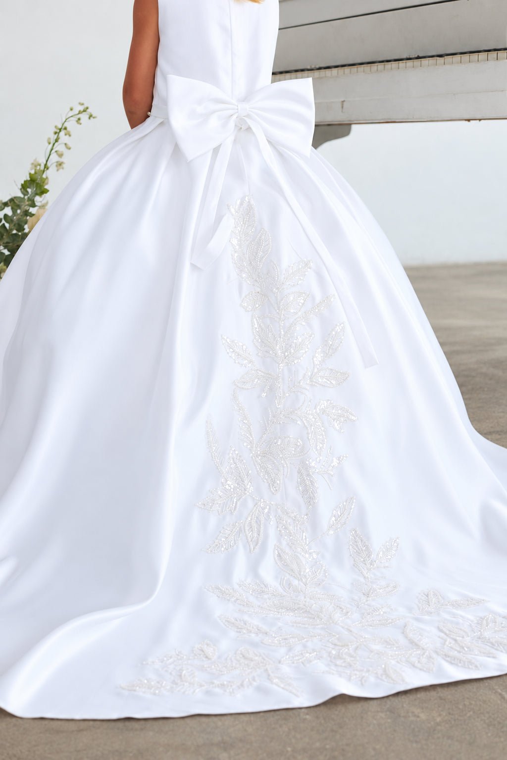 Close-up of the large satin back bow and beaded floral train on Tiptop 5925 white flower girl dress.