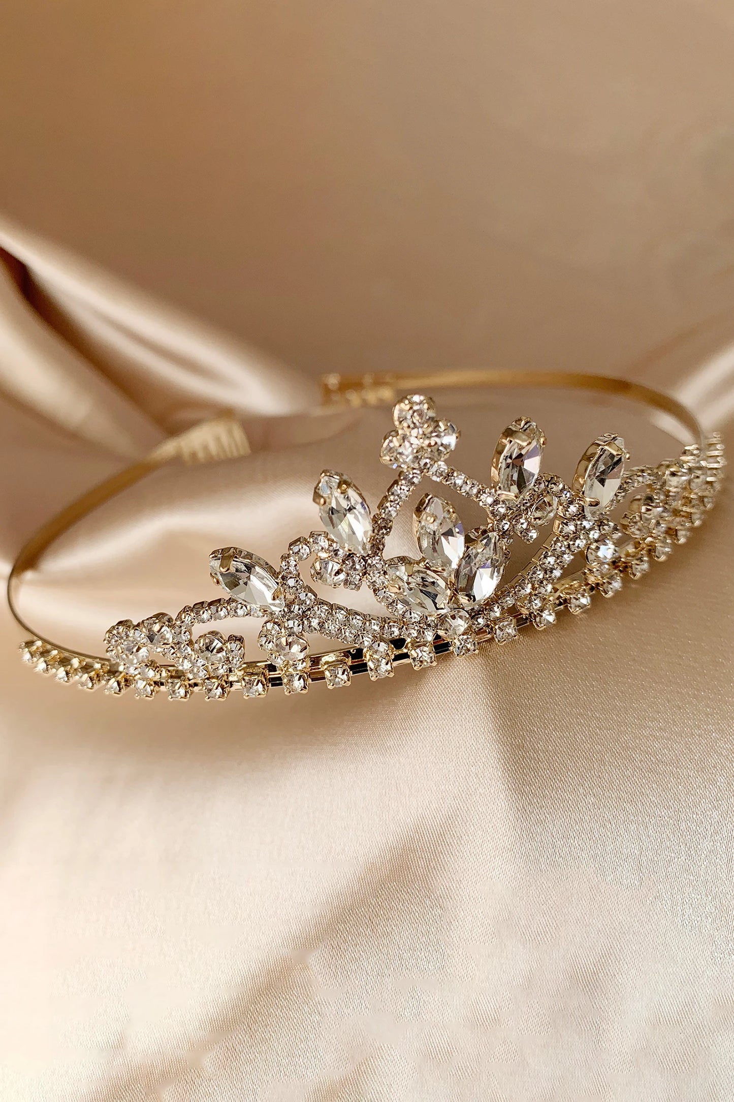 Gold tiara with dainty crystals on a beige satin background