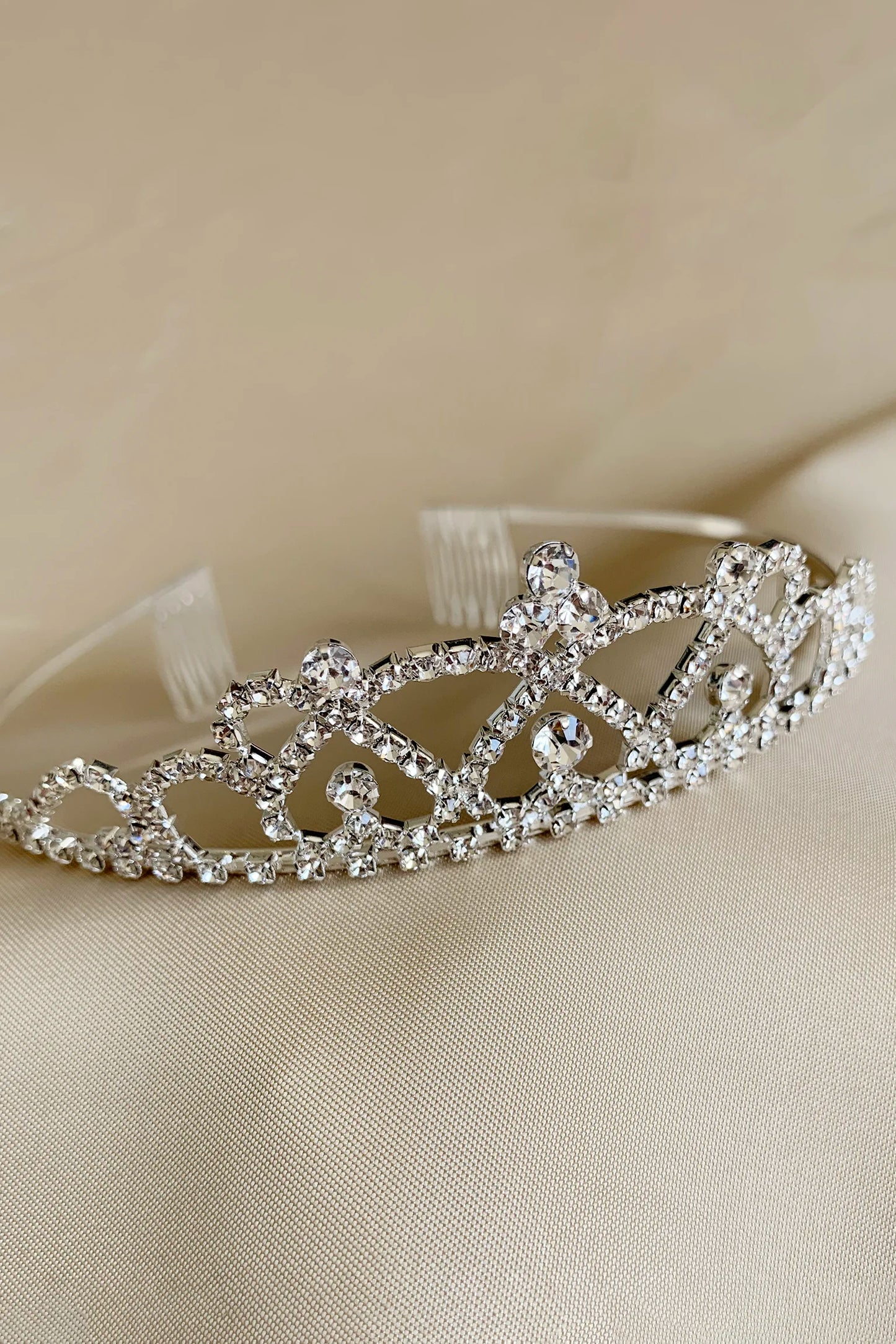 Silver clear rhinestone kid tiara on a beige fabric background