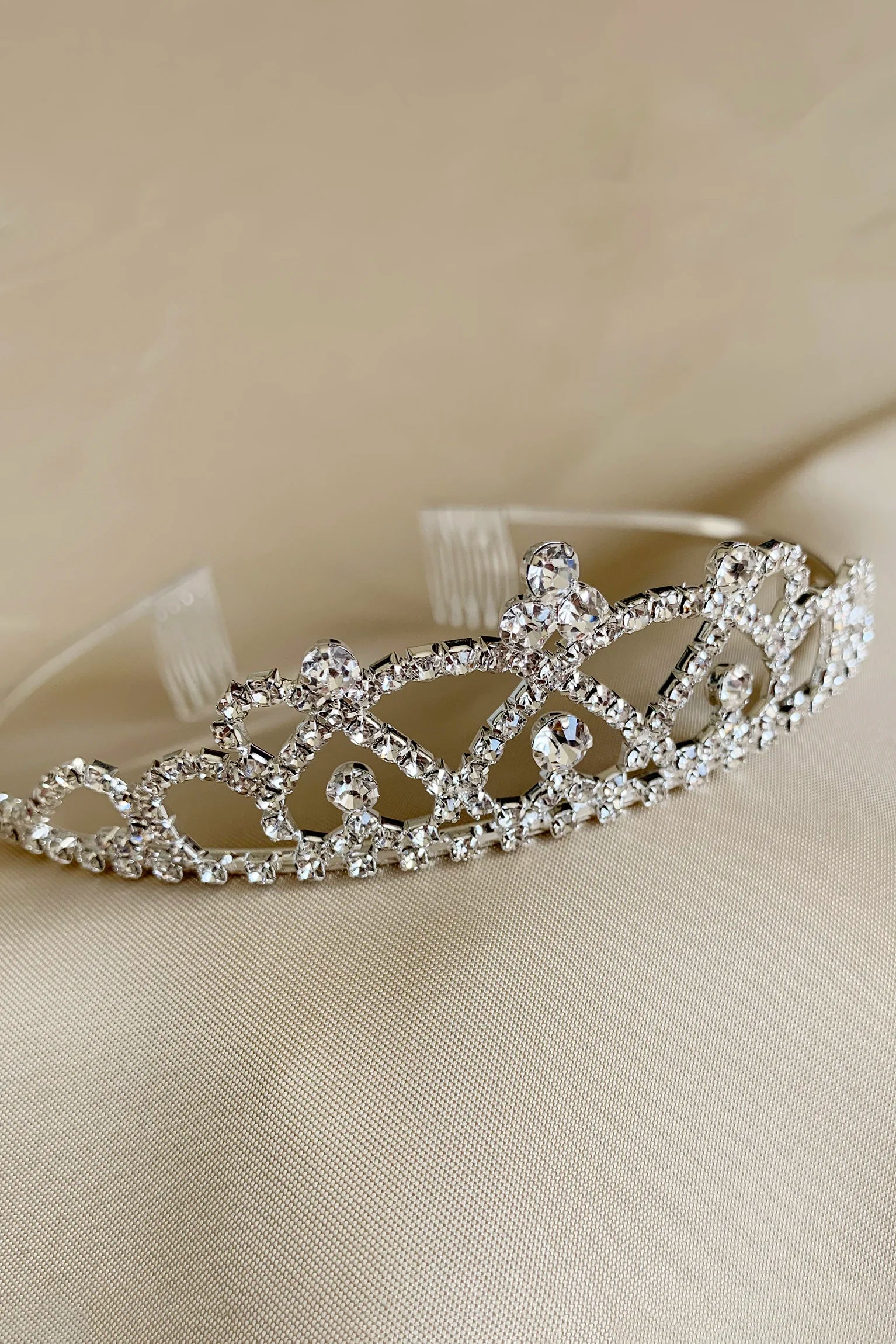 Silver clear rhinestone kid tiara on a beige fabric background