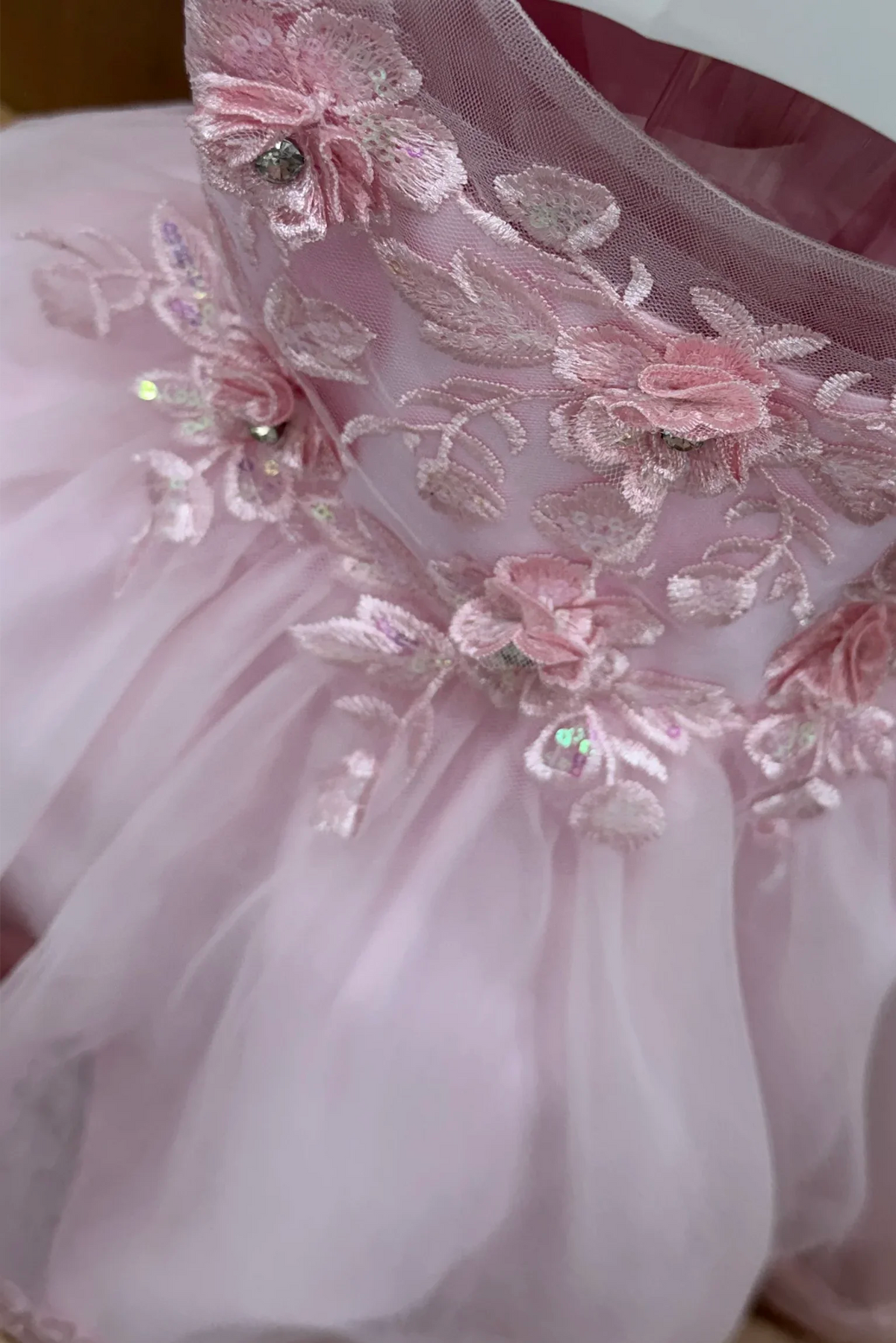 Close-up of a light pink tulle dress with floral embroidery and sequined details on the bodice.