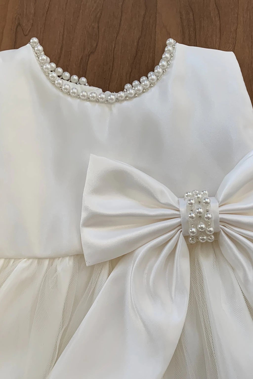 Ivory flower girl dress with a large bow and pearl details.