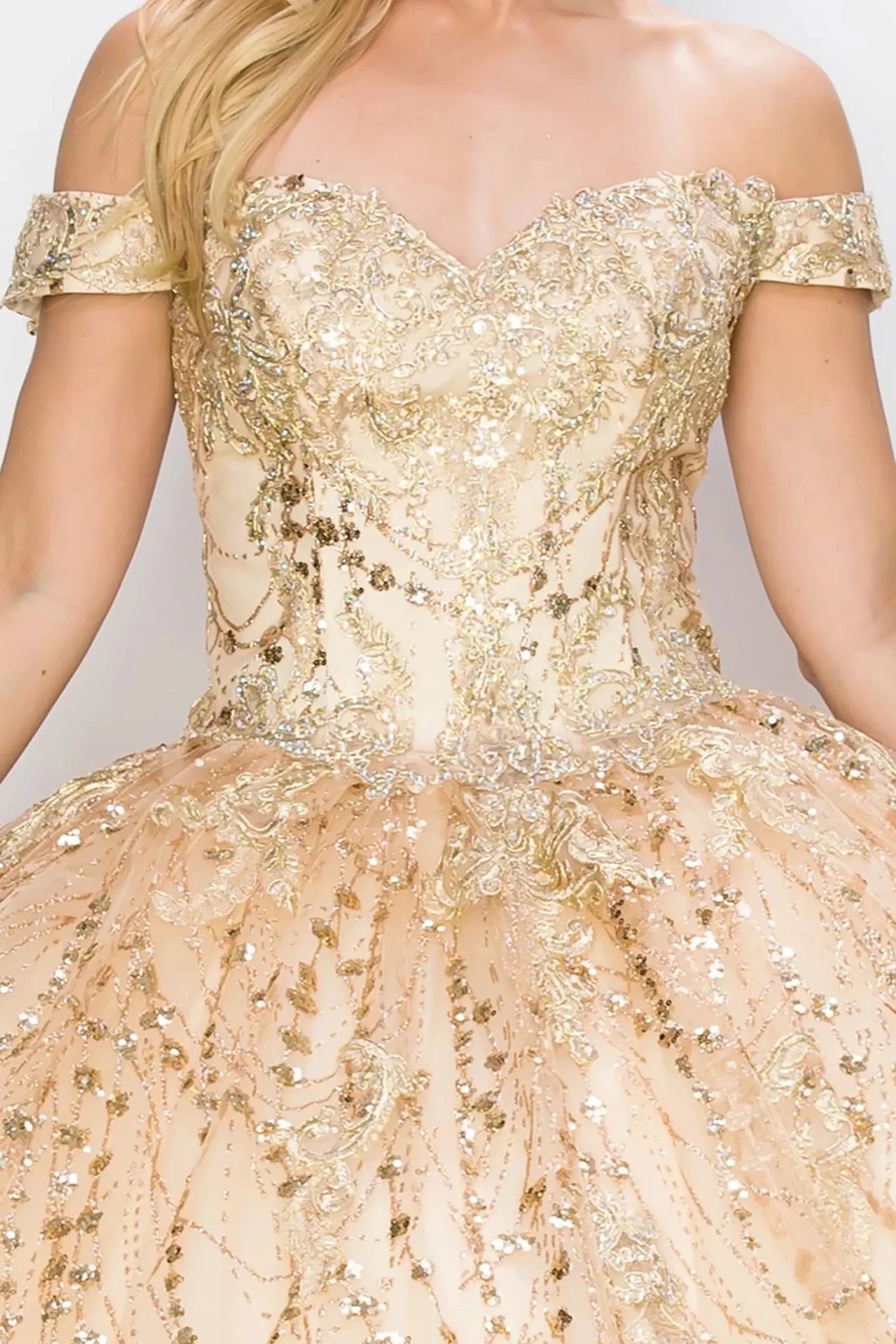 Front zoom view of a woman wearing champagne quinceanera ball gown with sweetheart neckline, gold embroidery, and glitter bodice