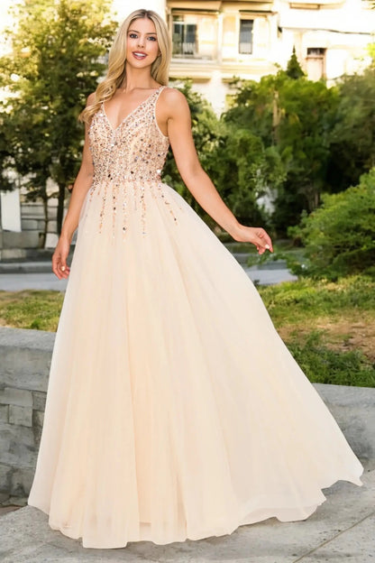A full-length front view of a woman wearing a champagne formal dress with an open V-neckline and flowing skirt.