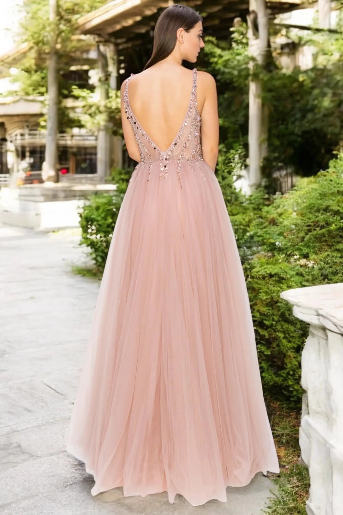 A full back view of a woman wearing a dusty rose formal dress featuring an open V-back design.
