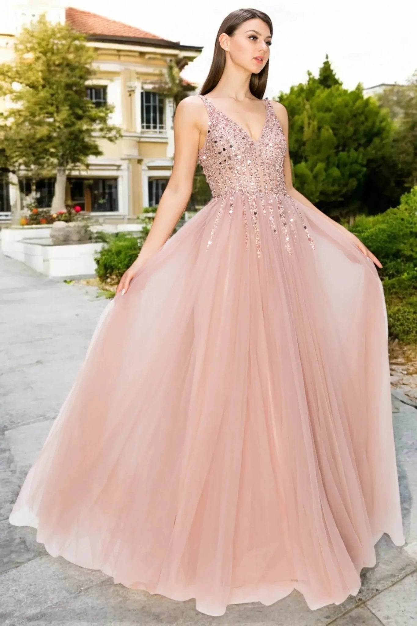 A full-length front view of a woman wearing a dusty rose formal dress featuring an open V-neckline design.