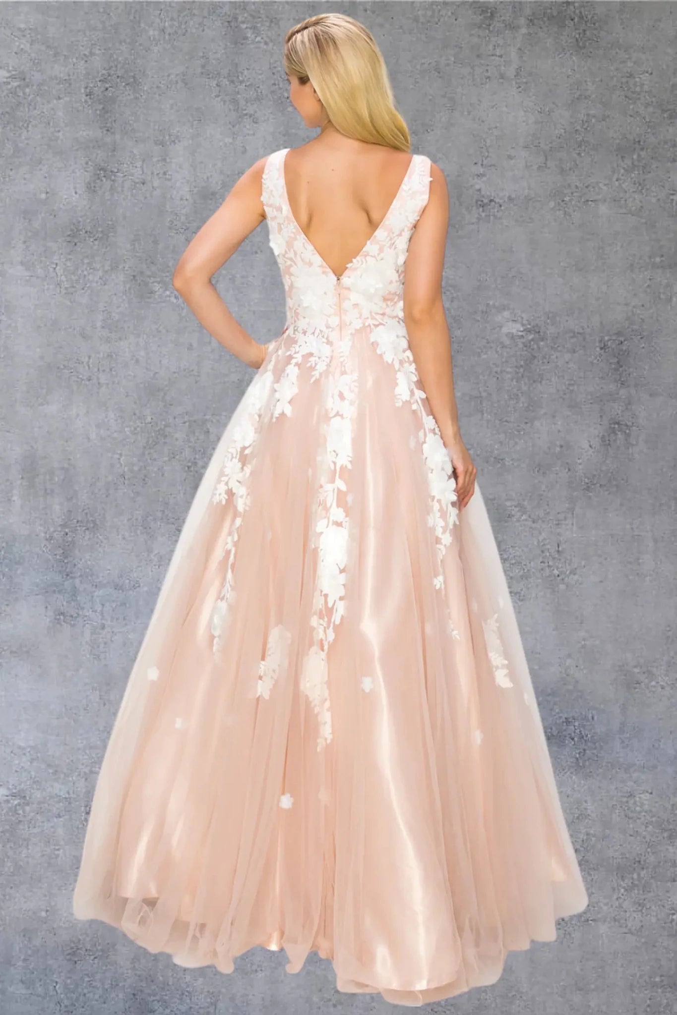 A full back view of a woman wearing a blush formal dress with a deep V-back and flowing skirt.