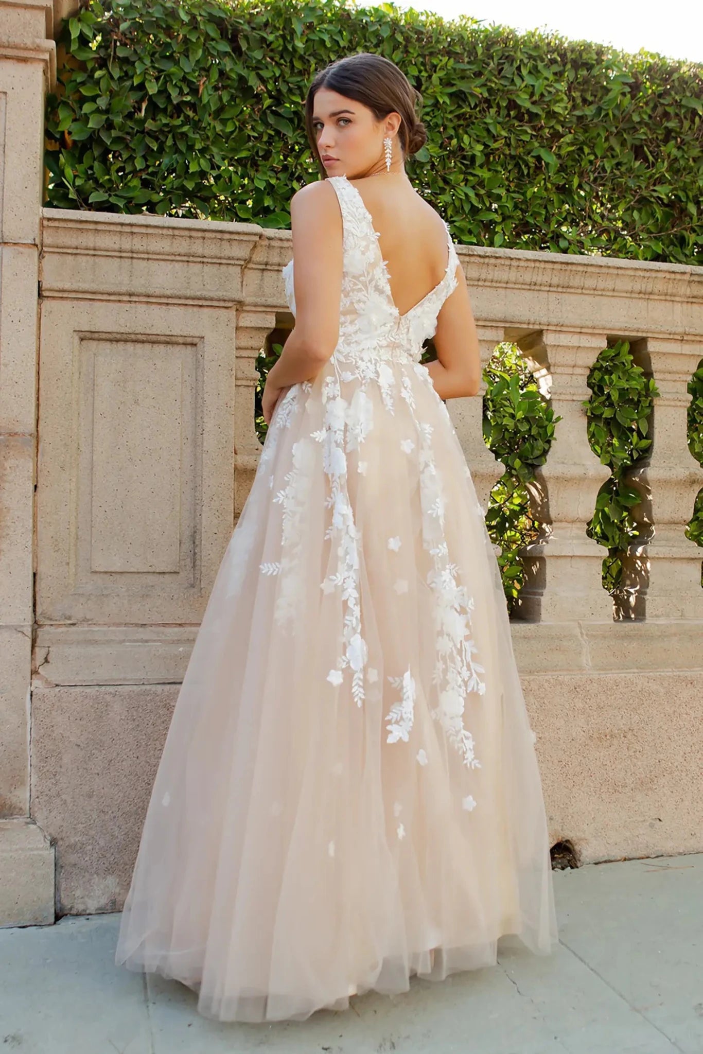 A full back view of a woman wearing a champagne formal dress with a deep V-back and A-line silhouette.