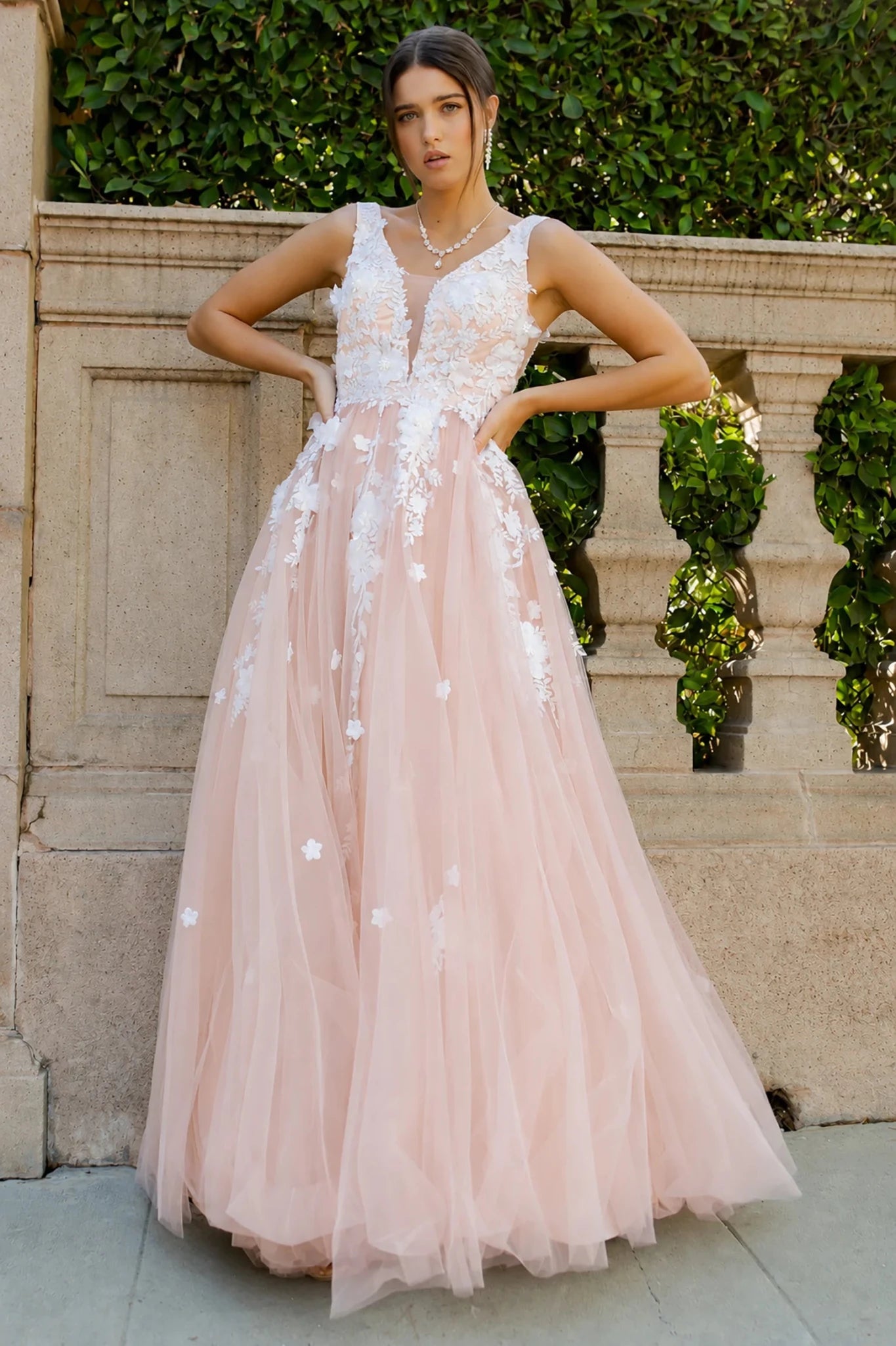 A woman models a sleeveless blush pink tulle dress with white floral lace appliques