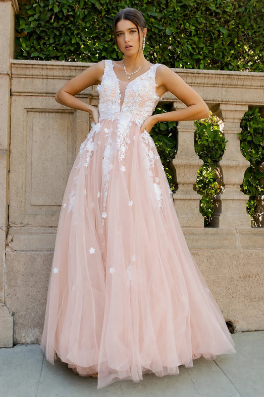 A woman models a sleeveless blush pink tulle dress with white floral lace appliques