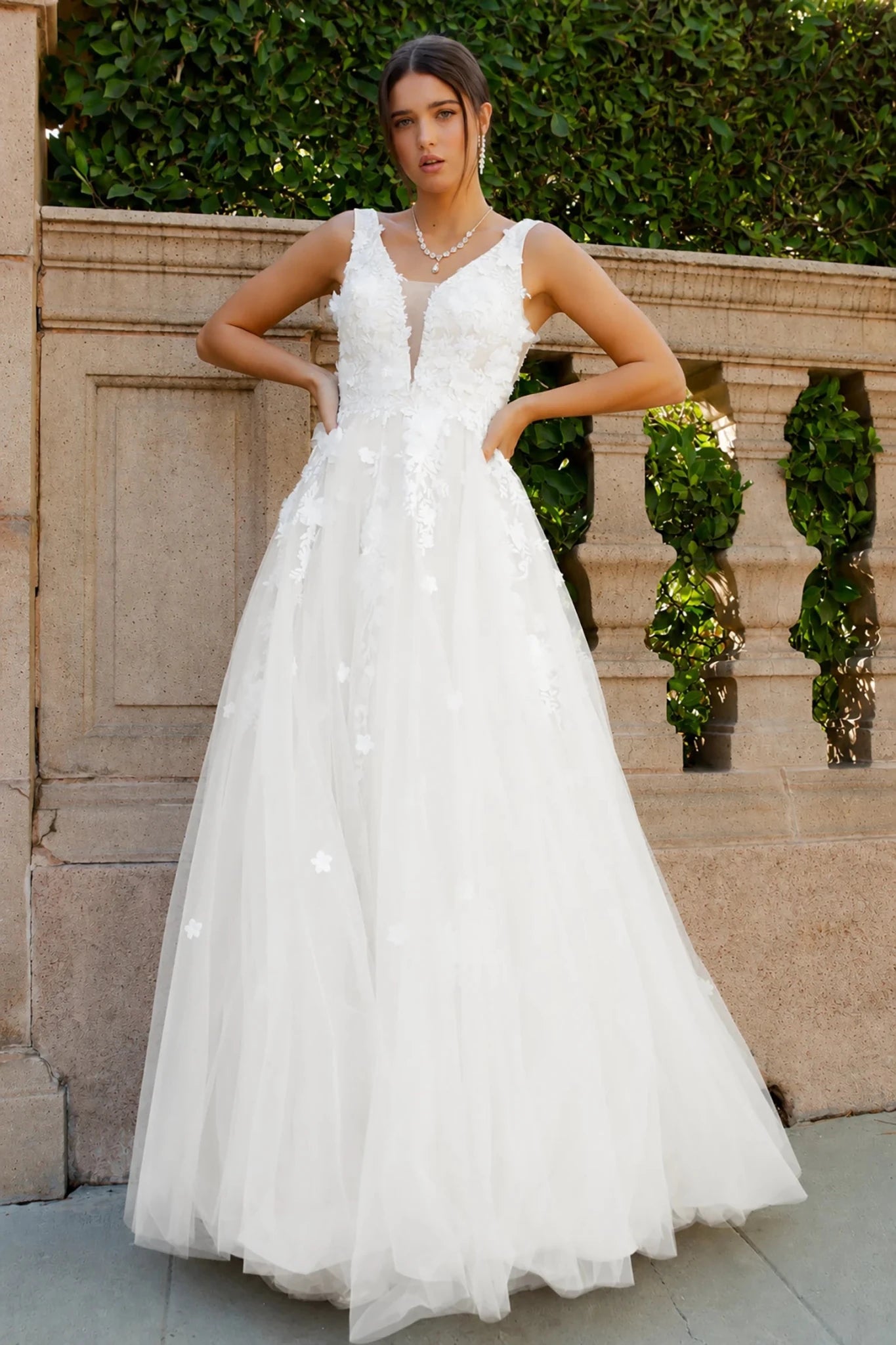 a sleeveless white wedding gown with a deep V-neckline, sheer lace bodice, and a full tulle skirt