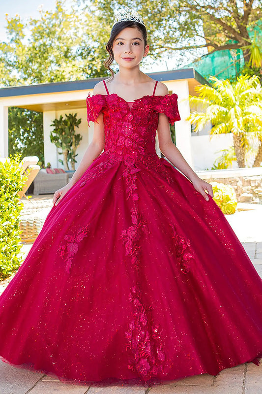Young girl standing front-facing in Adriana mini quinceañera dress with sweetheart neckline, 3D floral sequin appliqués, glitter lace bodice, and layered skirt with flowing train