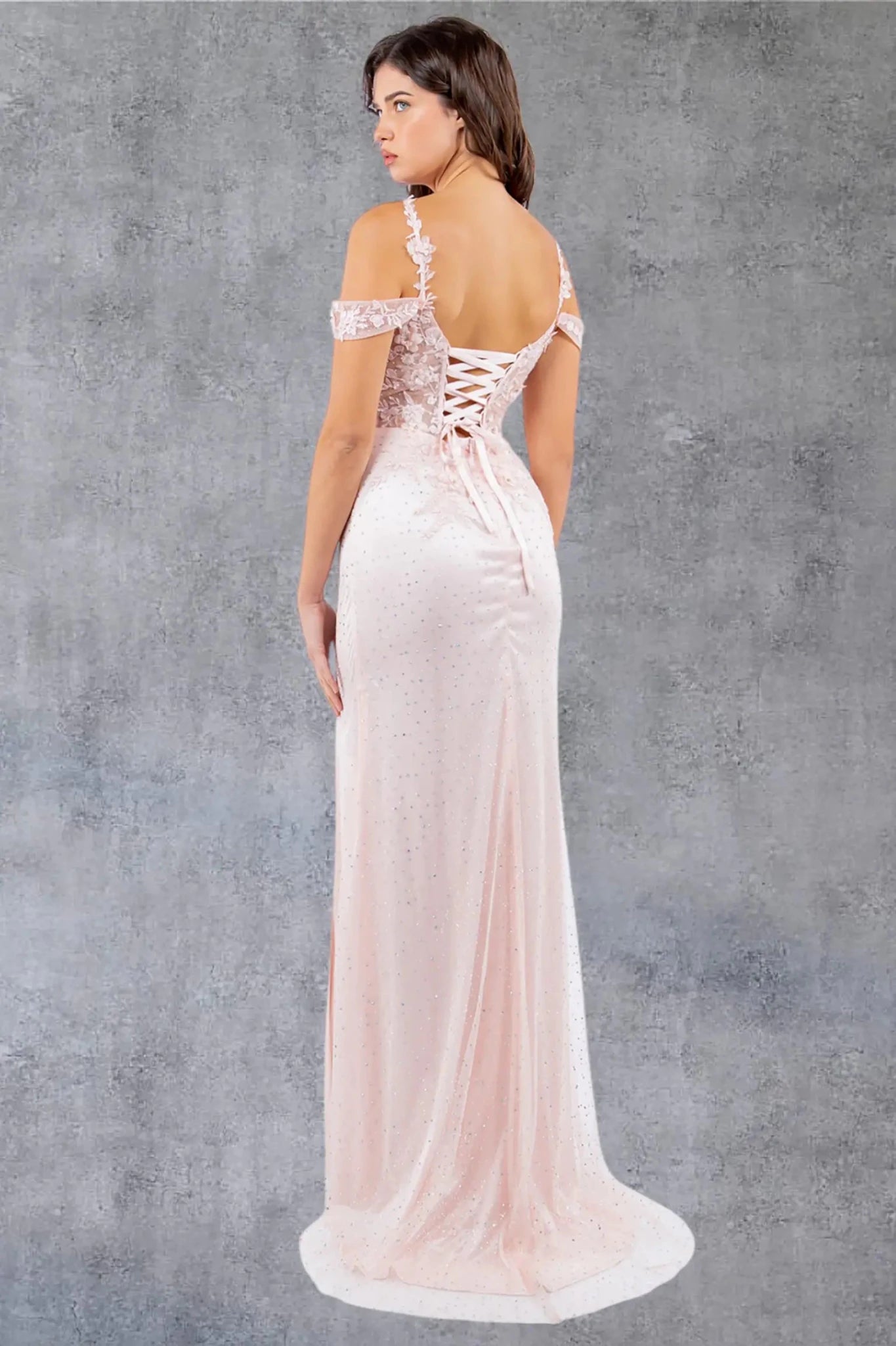 A full back view of a woman wearing a blush formal dress with a lace-up corset and detachable sleeves.