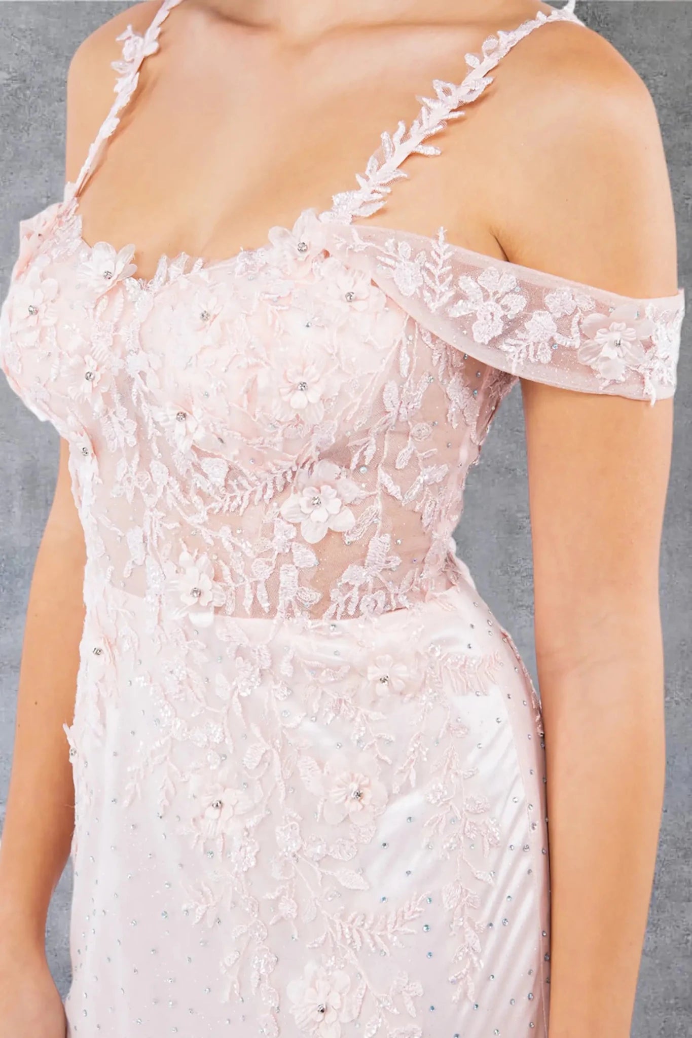 A close-up view of a woman wearing a blush off-shoulder bodice with rhinestones and floral appliqué detail.