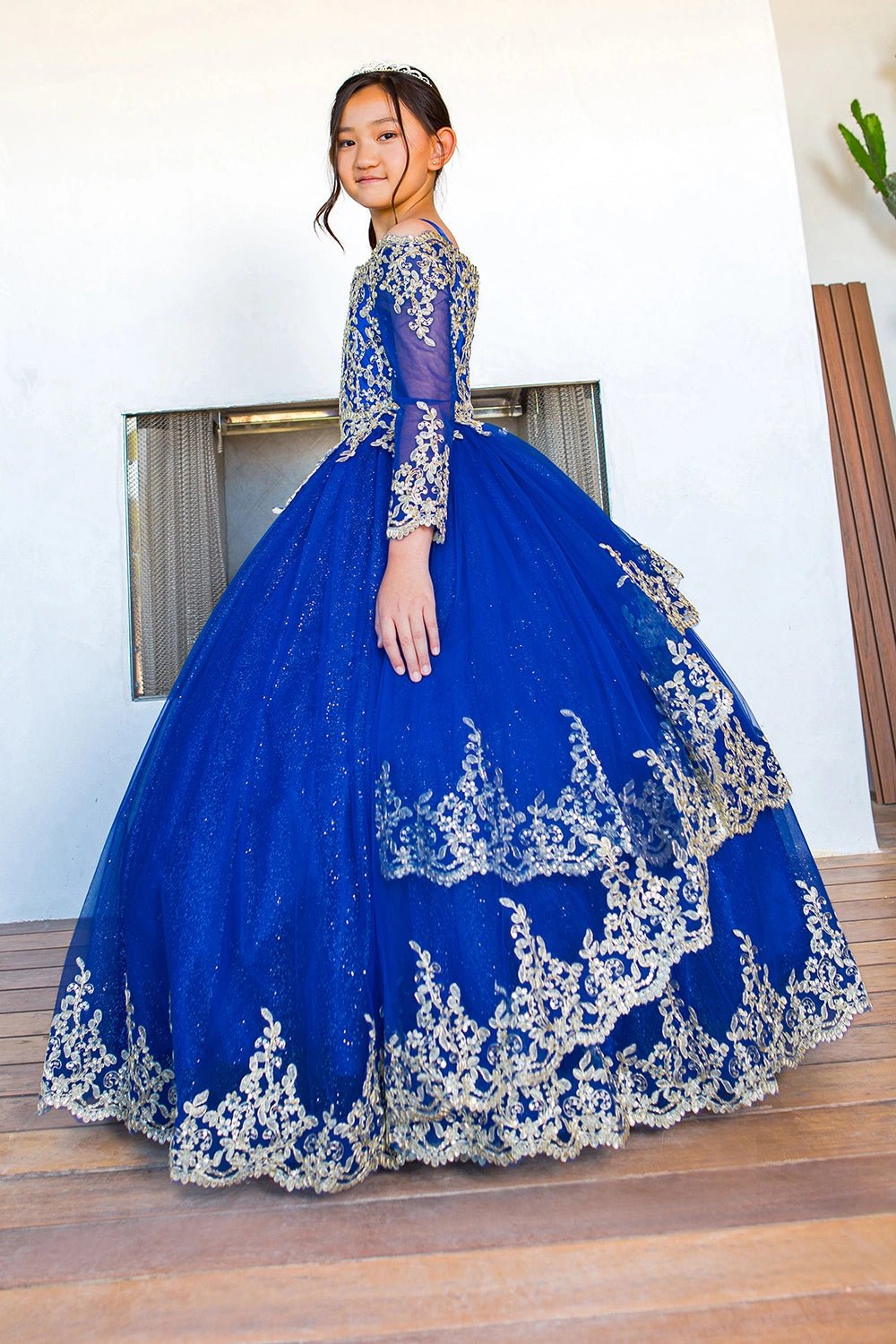 Displayed in a angled view, the Royal Blue mini quince dress has long lace-trimmed sleeves and layered glitter skirt.