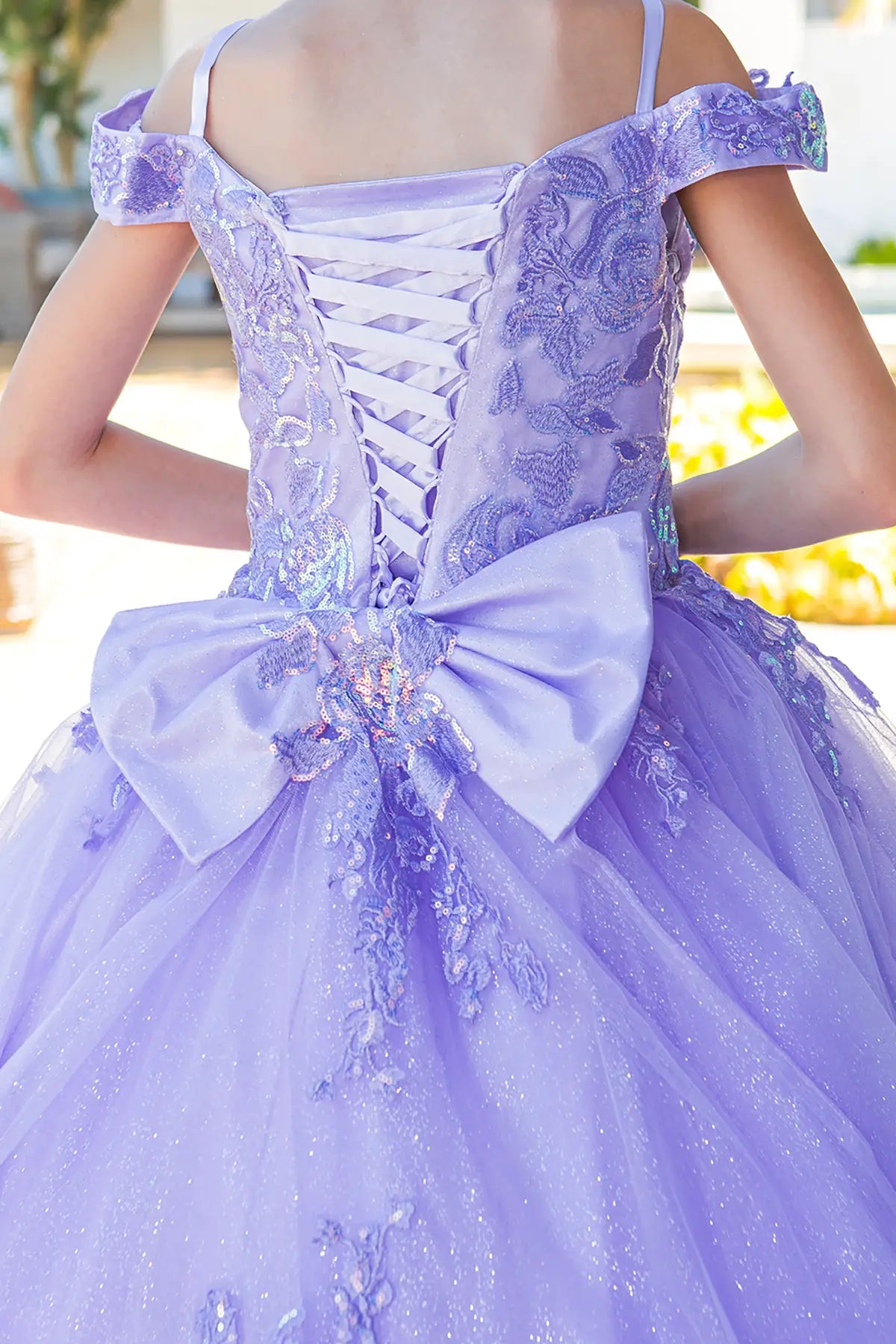 Lilac back view kids mini quinceañera mini quince dress with off-shoulder lace, floral embroidery and large bow detail.