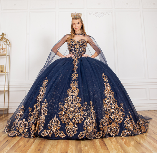 Woman wearing a navy blue evening gown with gold embroidery in a room with white walls and wooden floor.
