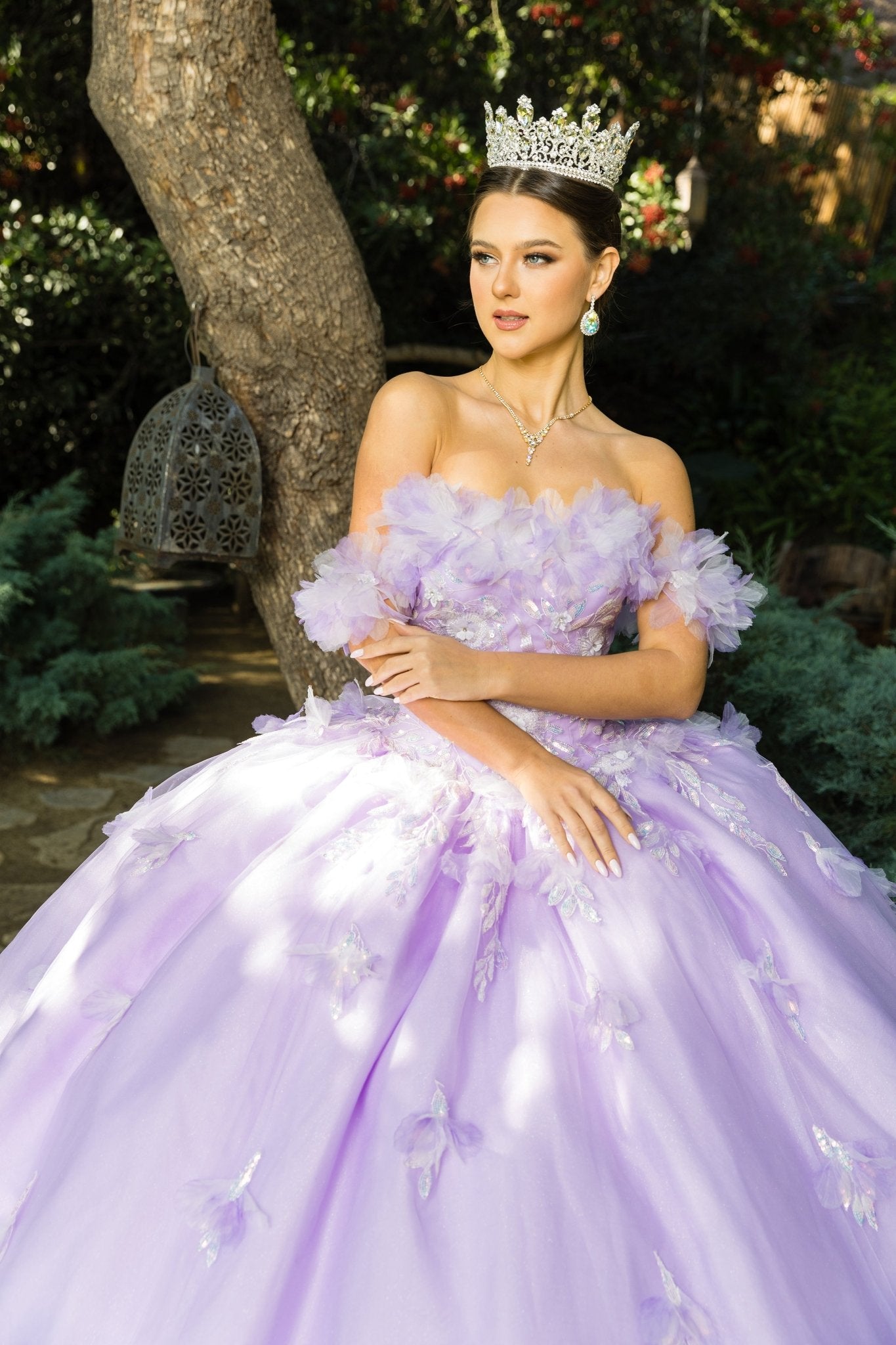 Front view of a woman wearing a lilac quinceanera dress with rainbow embroidery, sequin ruffle flowers, and crown detail