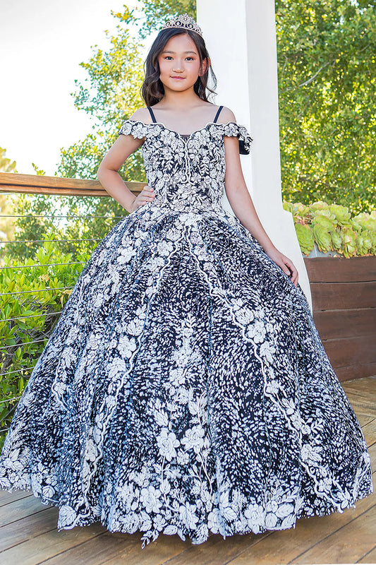 Young girl side-facing close-up in black and white Aitana mini quinceañera dress with off-shoulder sleeves, glitter tulle fabric, and intricate 3D floral appliqués
