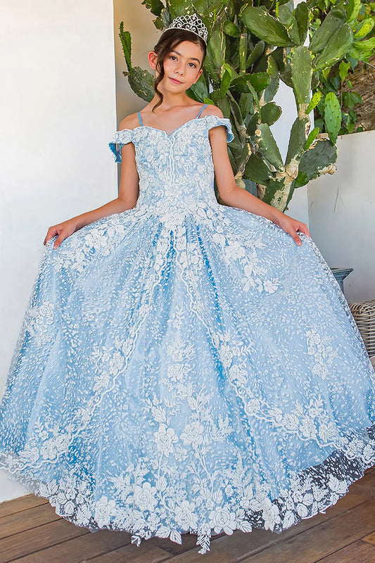 Young girl standing front-facing in blue and white Aitana mini quinceañera dress with off-shoulder sleeves, glitter tulle fabric, 3D floral appliqués, and elegant A-line skirt