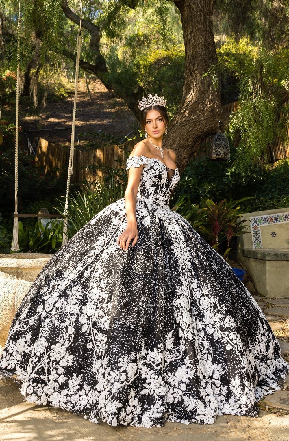 Presented in a angled view, the Black quinceañera dress has white floral lace appliques across the full skirt.