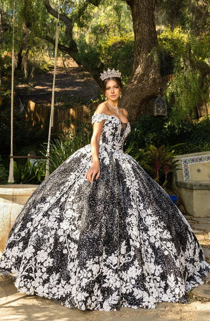 Presented in a angled view, the Black quinceañera dress has white floral lace appliques across the full skirt.