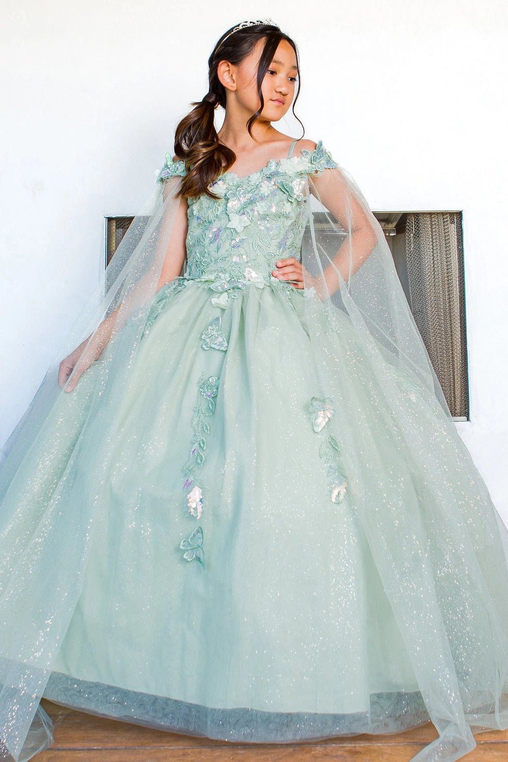 Shown in a front view, the Sage mini quince dress has floral bodice and sheer shoulder drapes over a glitter skirt.