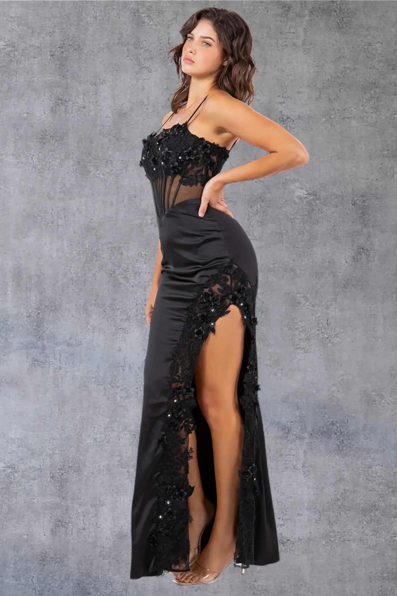 A side profile view of a woman wearing a black sequin prom dress, highlighting the fitted silhouette and slit detail.