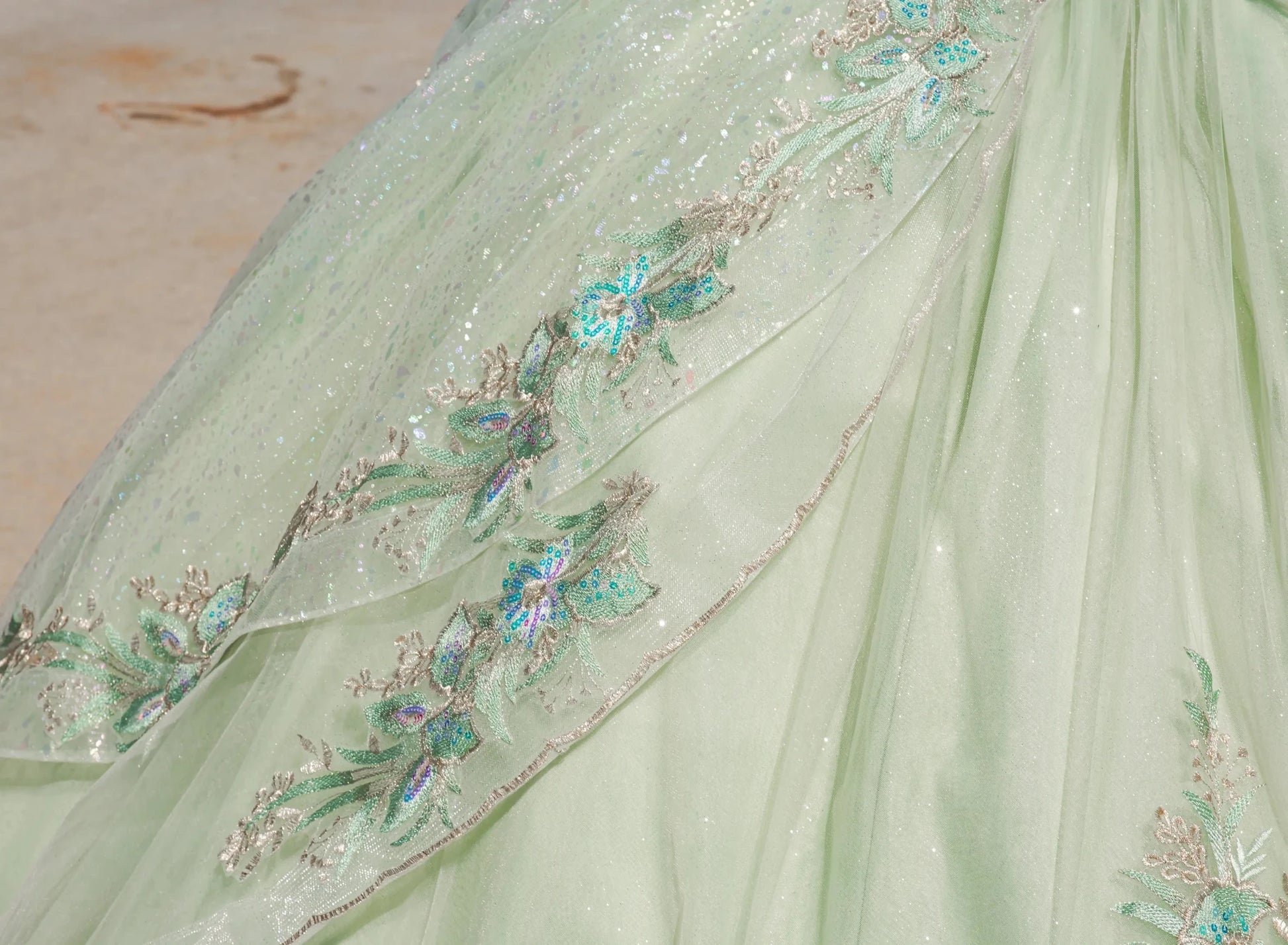 Light green fabric with floral embroidery and sequins on a neutral background