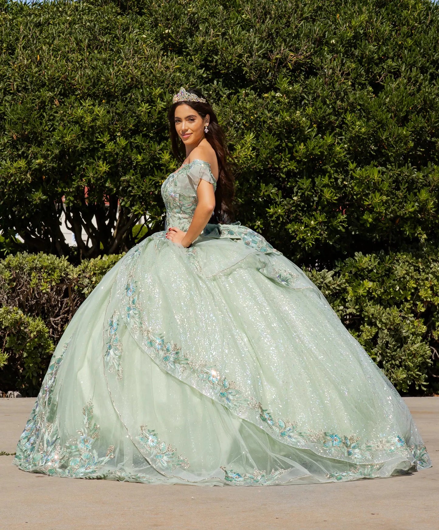 Woman in a light green quinceañera dress with floral details standing outdoors.