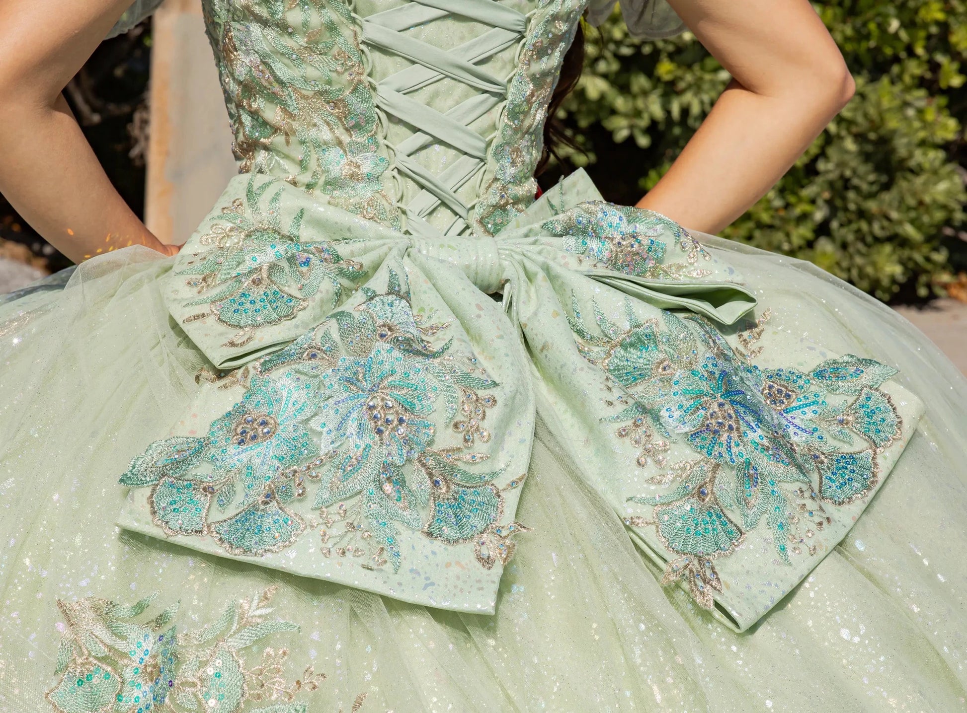 Close-up of a light green dress with floral embroidery and a large bow.