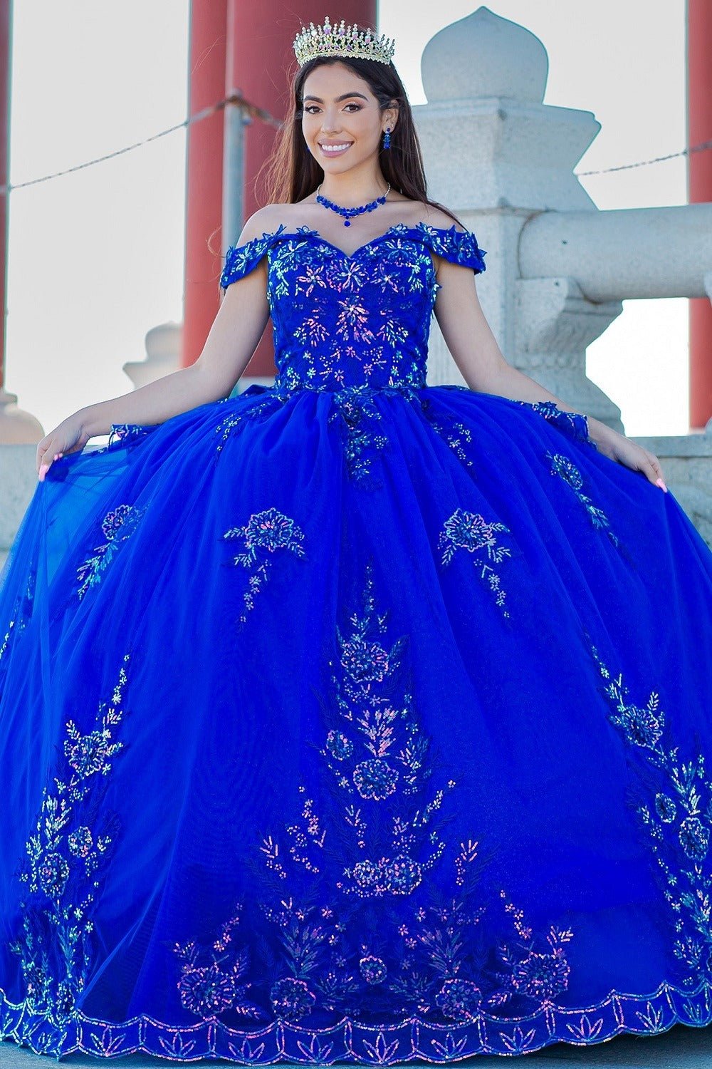 Front view of a woman wearing a blue quinceanera dress with floral embroidery, beaded appliques, and glitter tulle