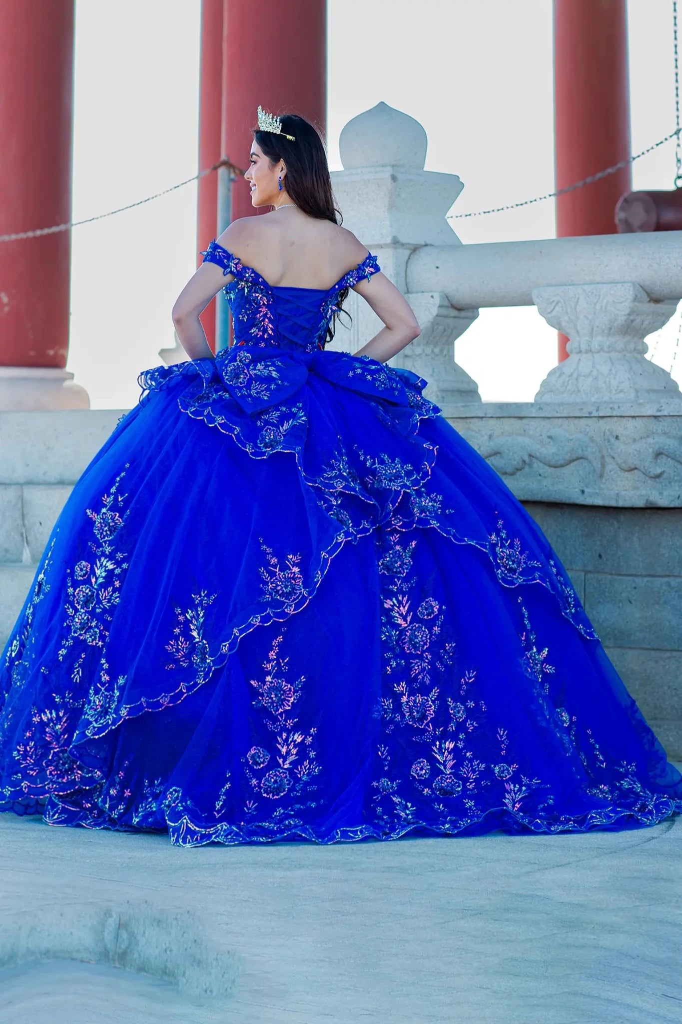 Back view of a woman wearing blue quinceanera gown with floral embroidery, beaded appliques, and long train