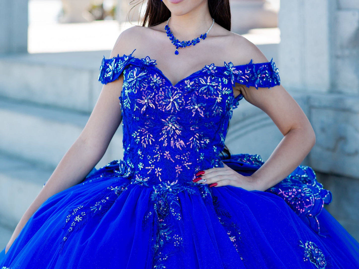 Front zoom view of a woman wearing blue quinceanera dress with off-shoulder beaded applique bodice and glitter tulle skirt