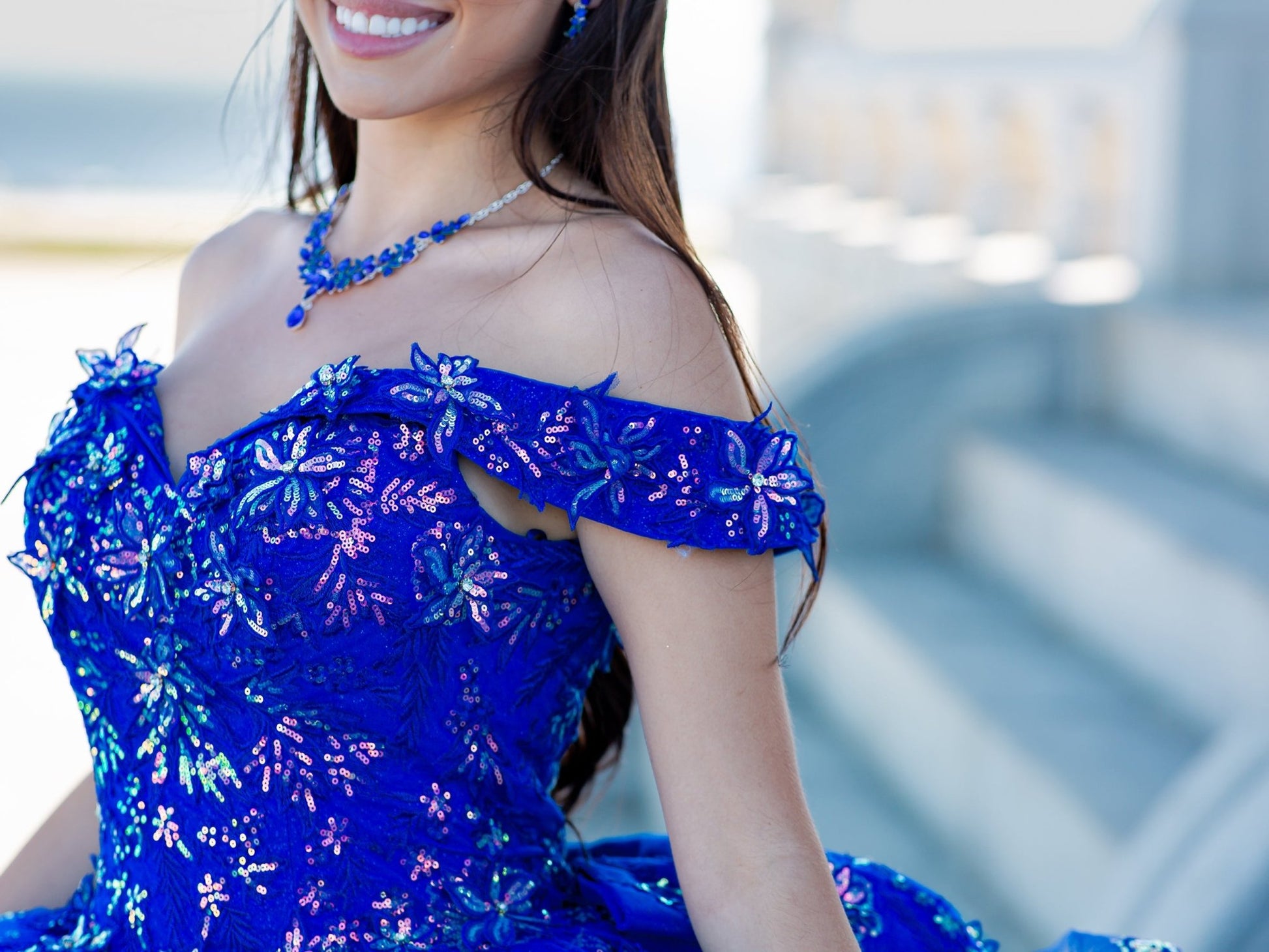 Front zoom view of a woman wearing blue quinceanera dress with sweetheart neckline, glitter 3D flowers, and beaded appliques