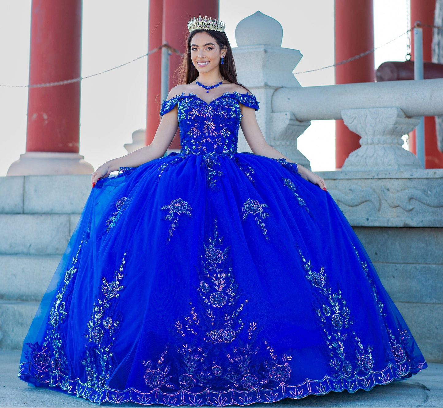 Full view of a woman wearing blue quinceanera dress with beaded applique bodice, glitter 3D flowers, and long train