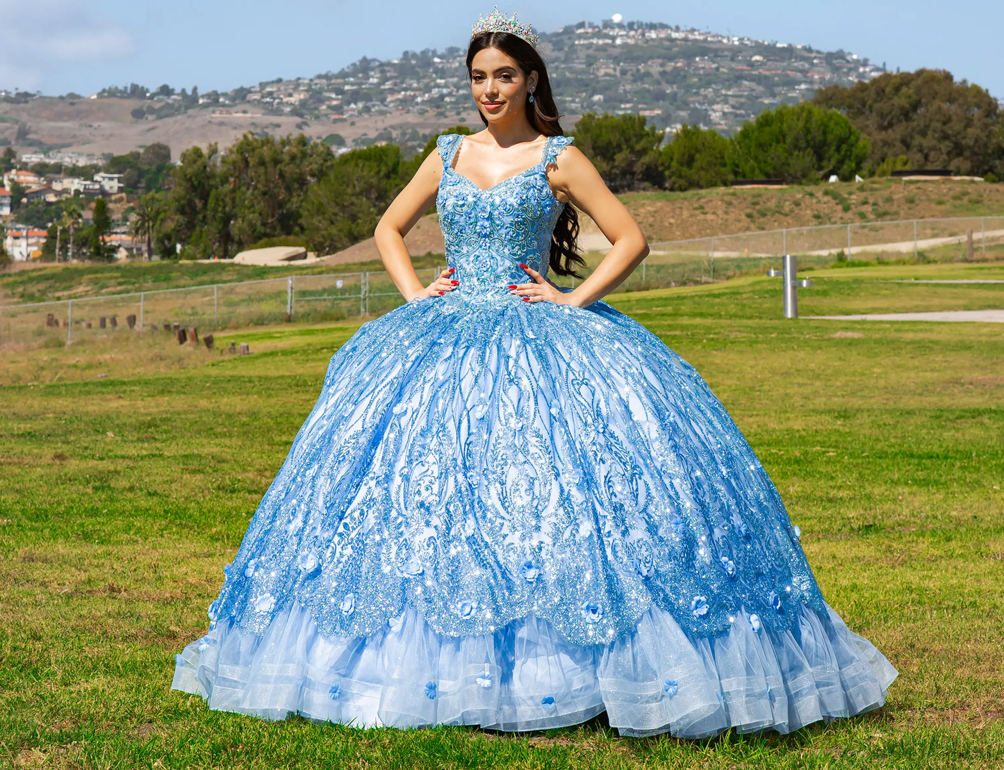 Woman in a blue quinceañera dress standing in a grassy field with mountains in the background