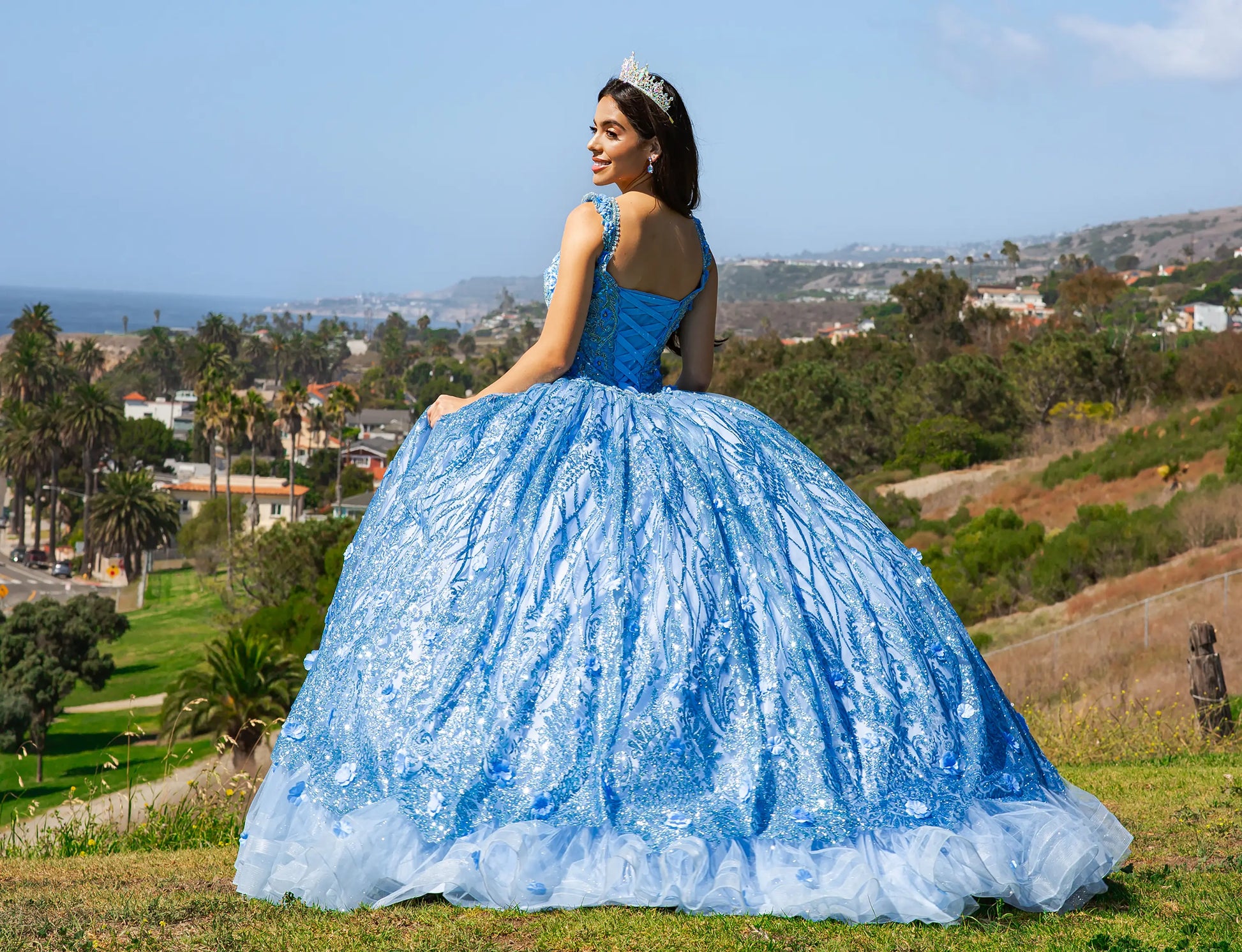 Woman in a blue quinceañera dress standing outdoors with a scenic background