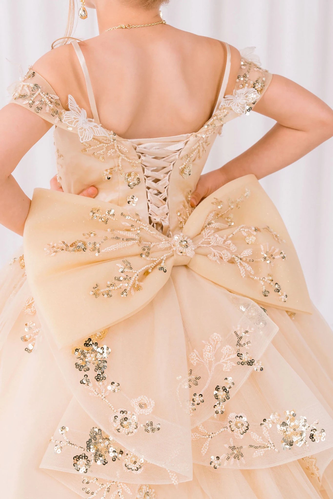 Champagne front view kids mini quinceañera mini quince dress with floral lace, bow detail and glitter tulle skirt.