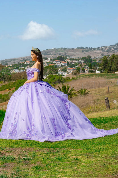 Woman in a lilac ball gown with fluffy skirt standing in a scenic outdoor setting with hills and trees.