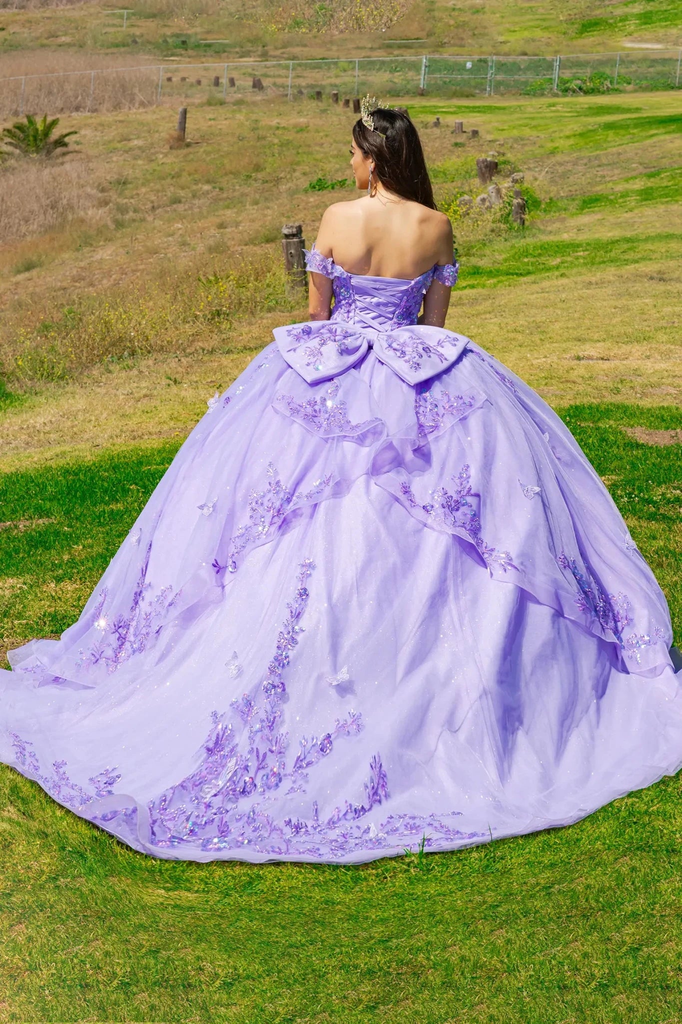 Person wearing a lilac ball gown showing her back of the dress with large big bow, lace up back and long train