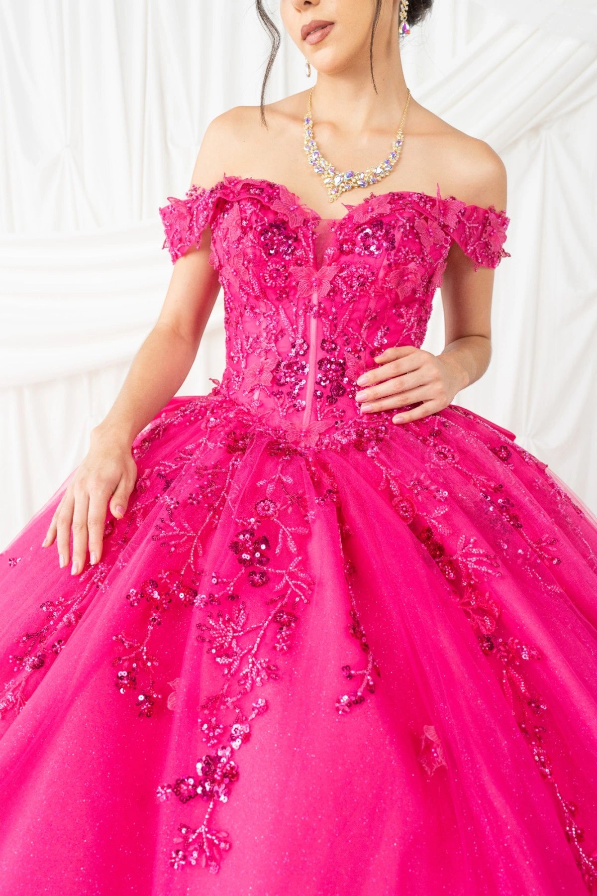 Presented in a bodice detail, the Fuchsia quinceañera dress has beaded floral bodice with off-shoulder sleeves.