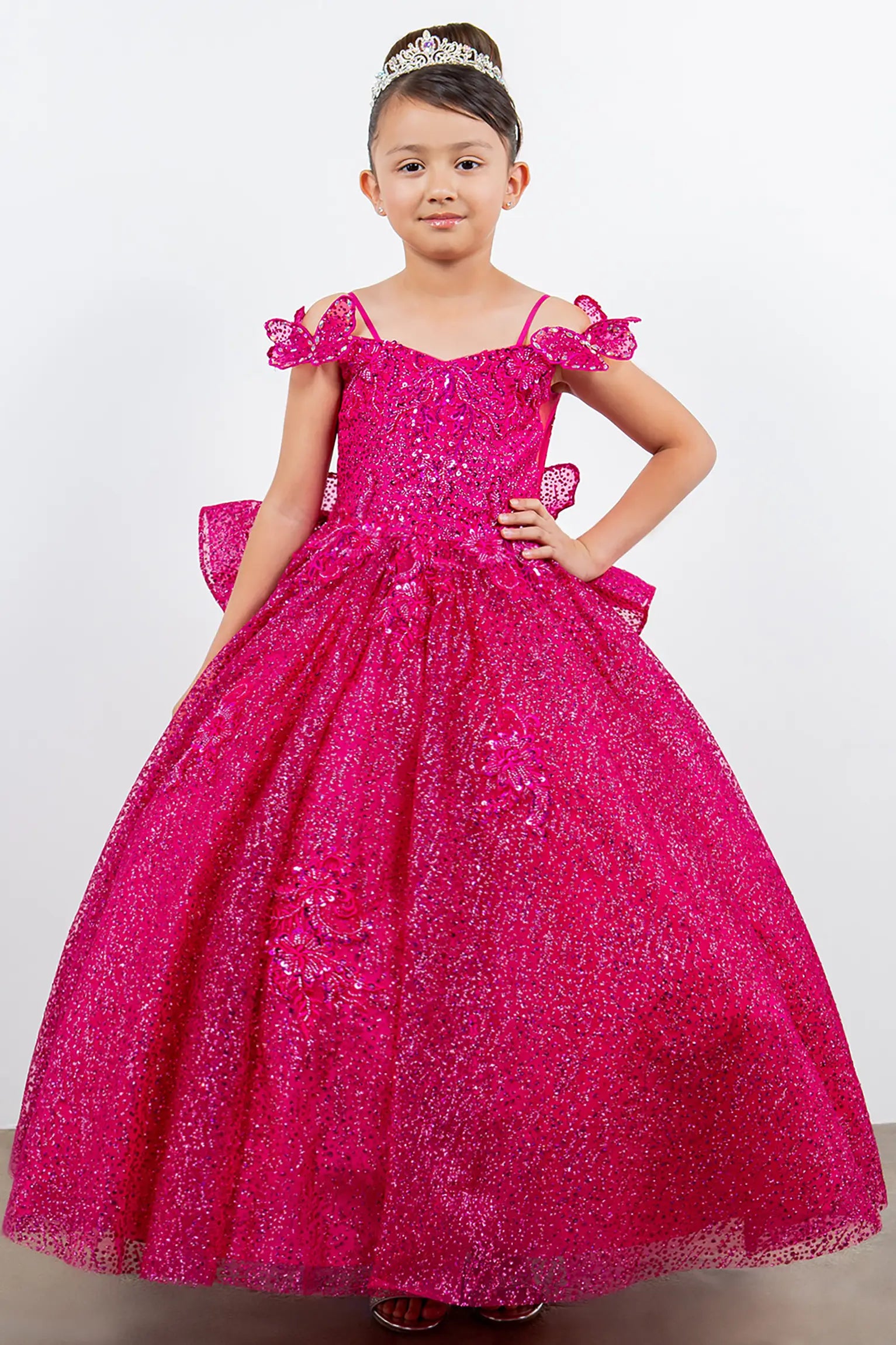 Young girl wearing a pink sparkly dress with ruffles on a white background | front full view