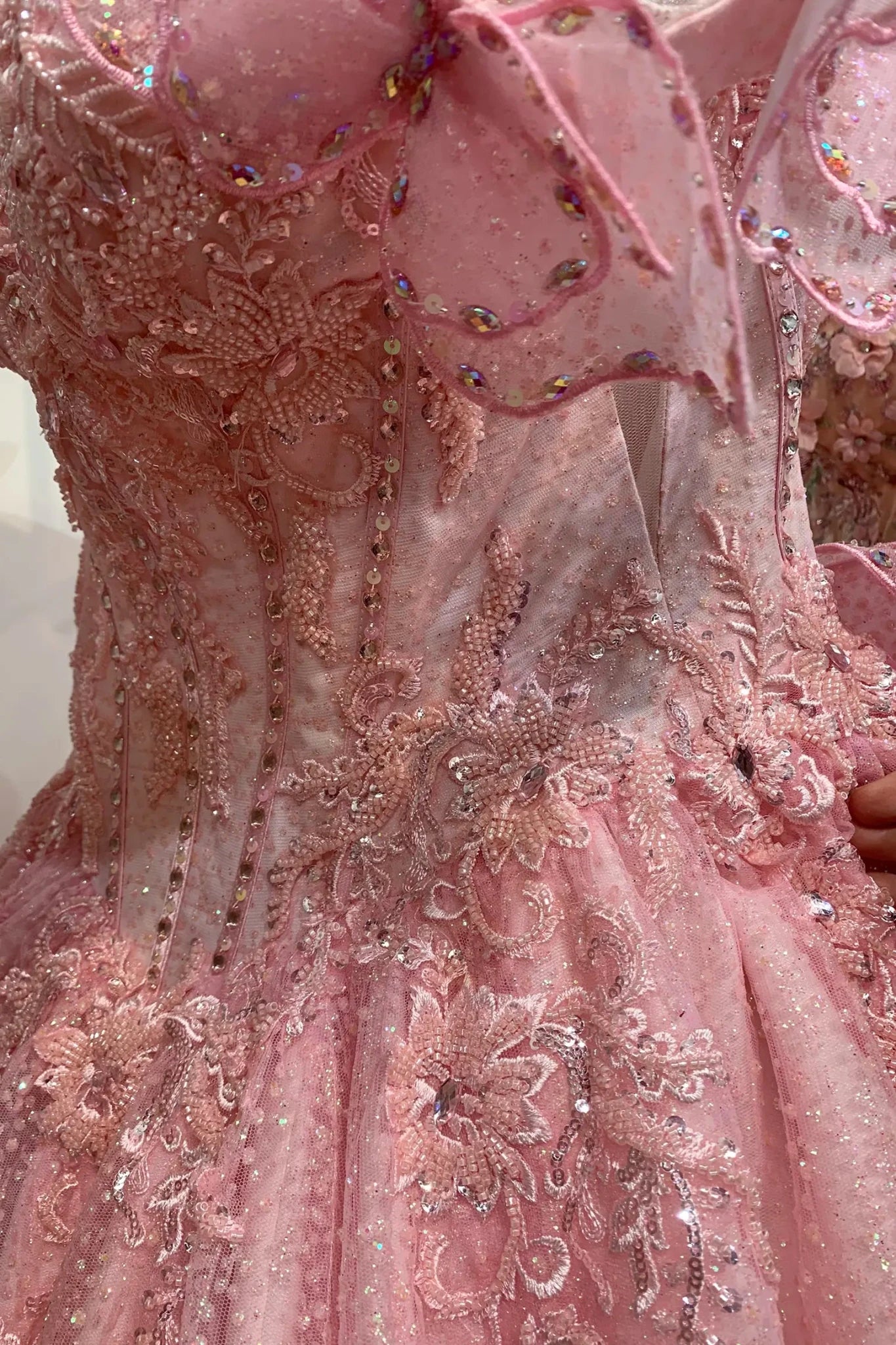 Blush quinceañera dress with dense all-over beading on the fabric and large butterfly appliqués decorating the sleeves.
