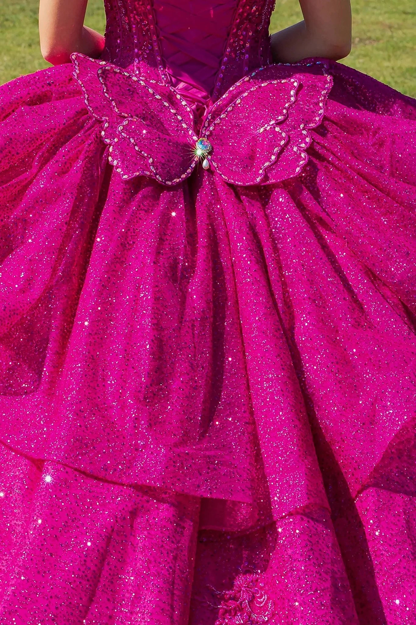 Close-up of a fuchsia pink glittery dress with a butterfly detail on a grassy background