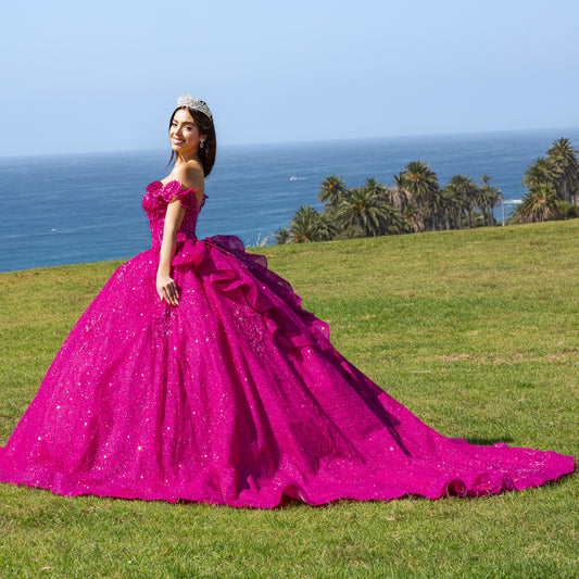 Woman in a fuchsia gown standing on grass with ocean and palm trees in the background