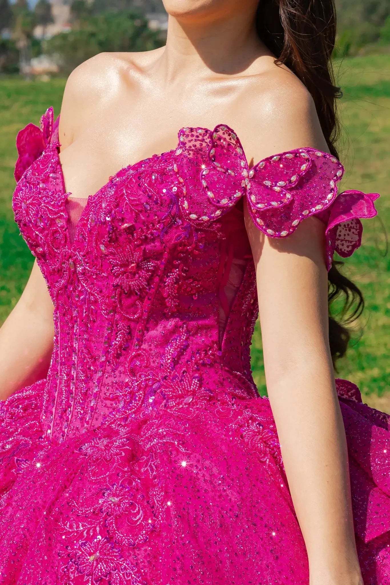 Woman standing close up in fuchsia hot pink ball gown with lace and sequin detailing, off-the-shoulder ruffled sleeves with butterfly
