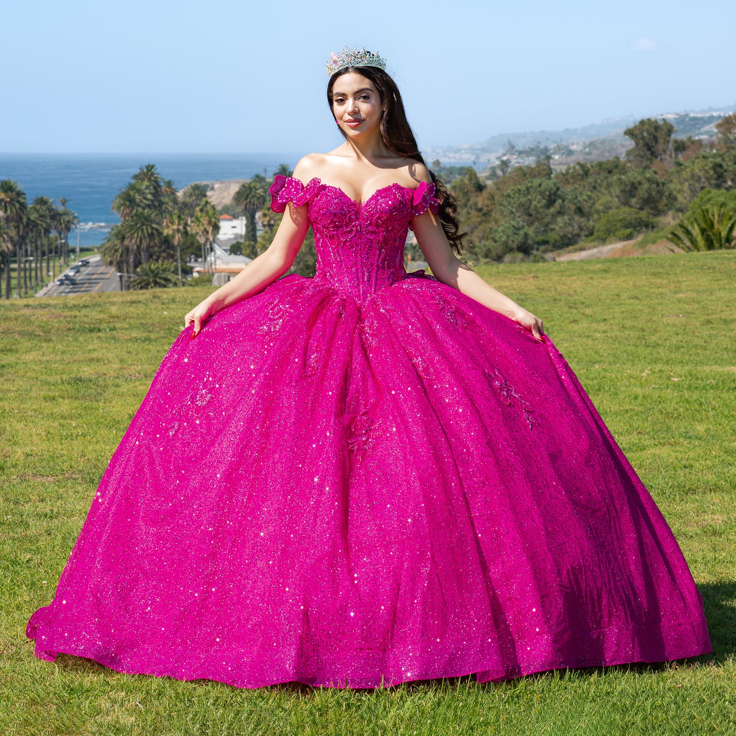 Woman in a fuchsia quinceañera dress standing on grass with ocean view