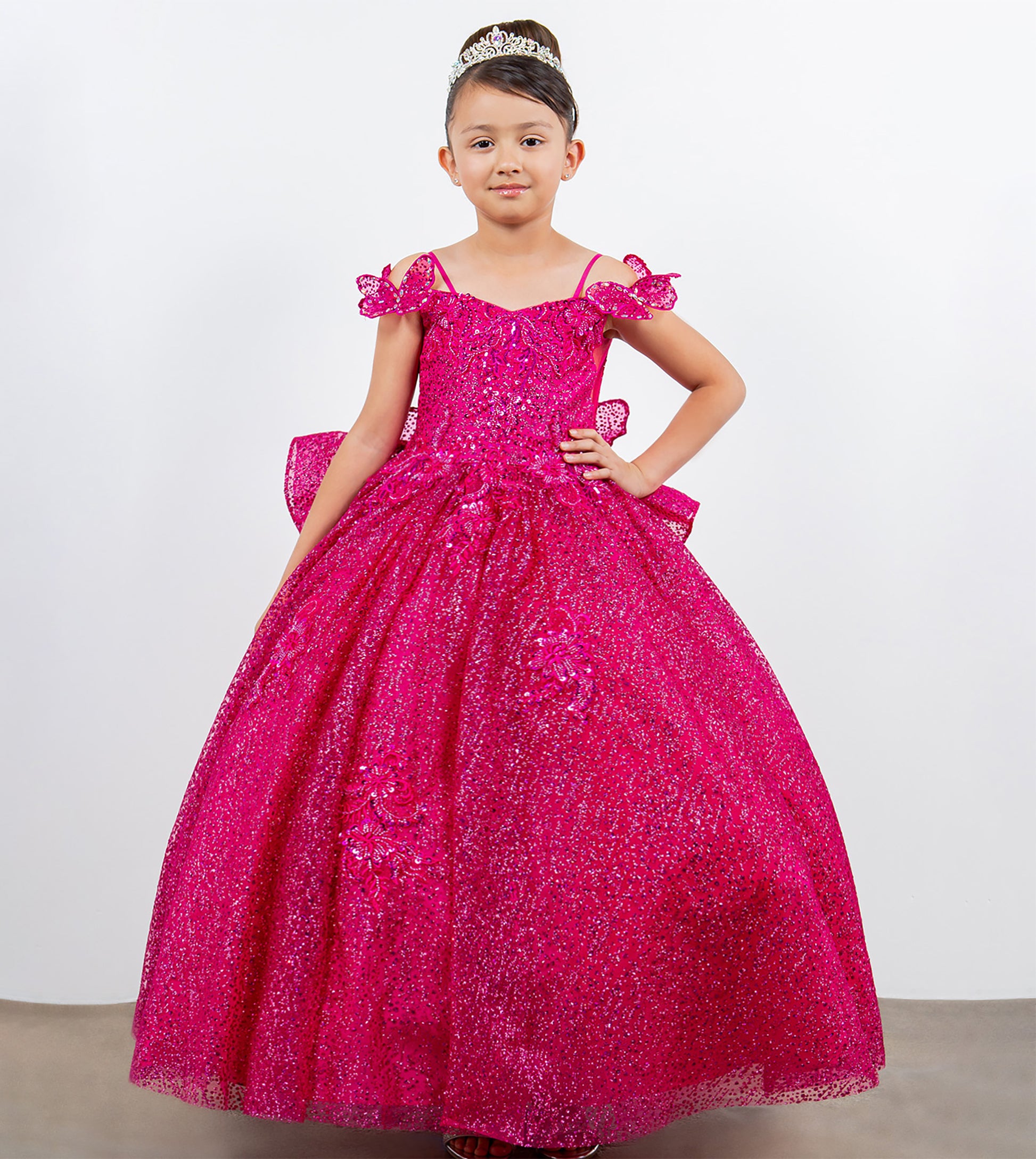 Young girl in a pink sparkly dress with a tiara on a plain background