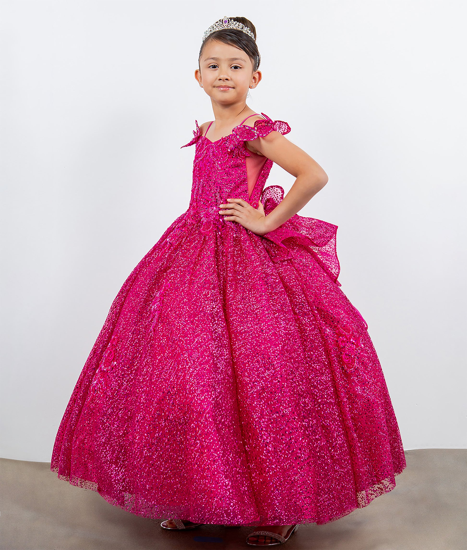 Young girl in a pink formal gown with a tiara on a plain background